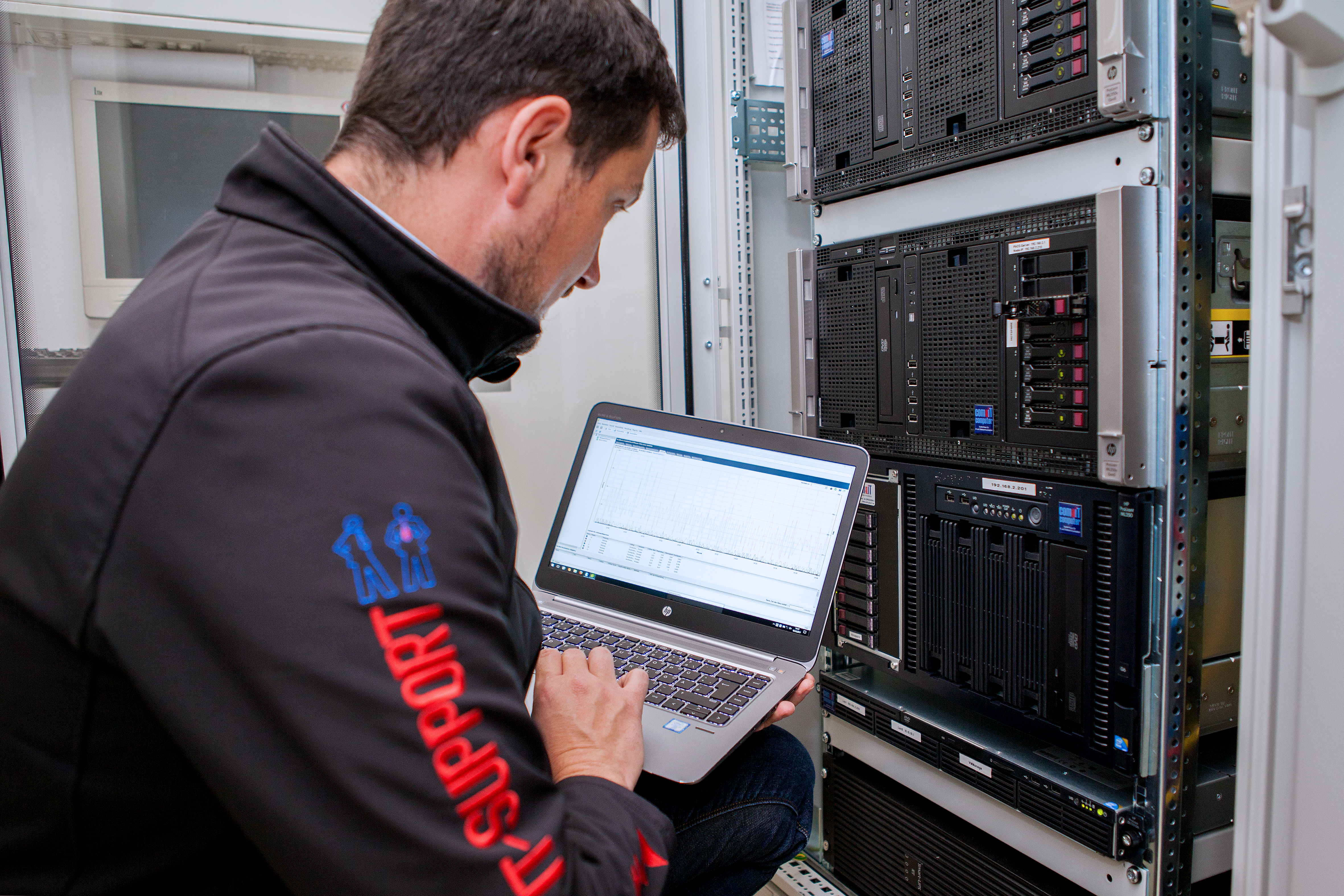Ein IT-Techniker prüft mit einem Laptop die Systeme an einem Serverrack.